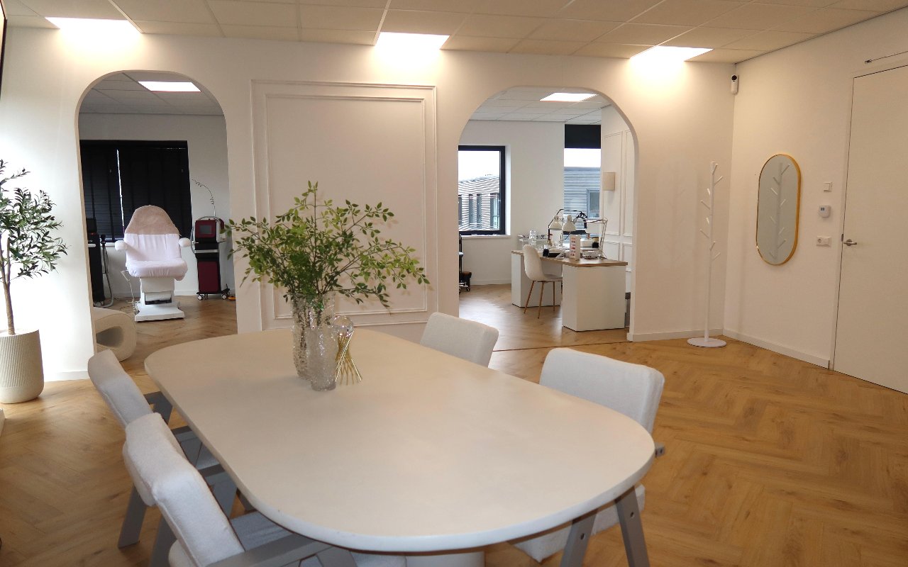 De salon: lichte ruimte met boogdoorgangen, een ronde witte tafel en de behandelstoel achterin